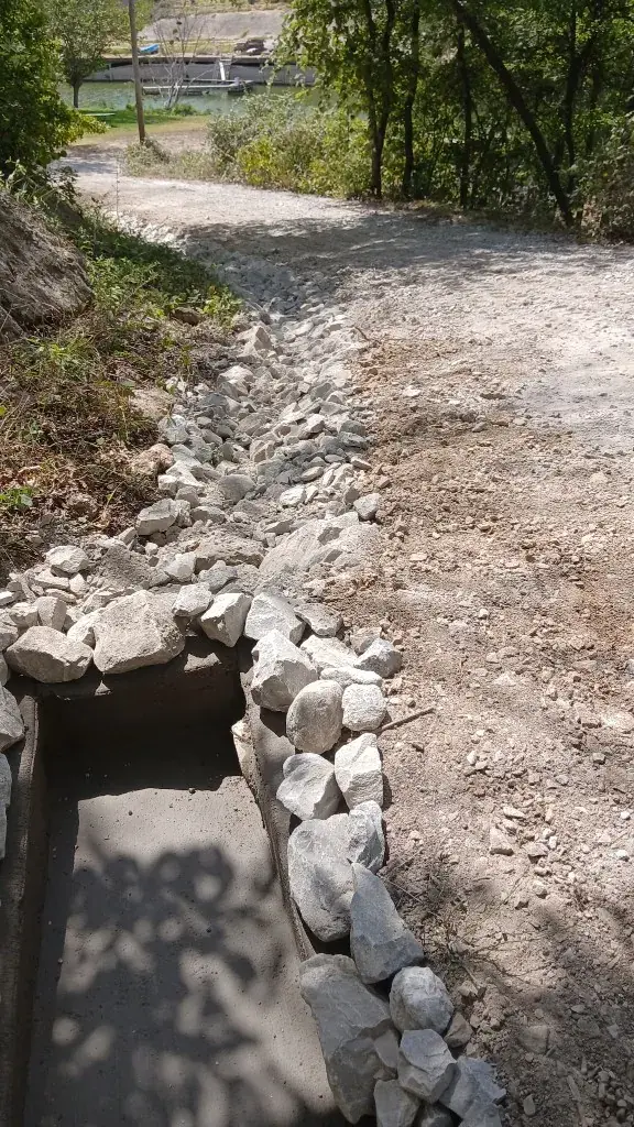 Riprap-lined drainage ditch feeding a catch basin beside a leveled gravel path