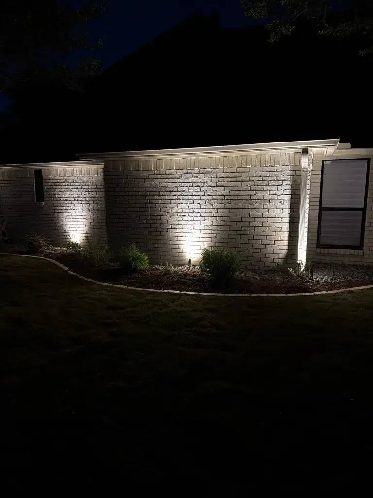 Southlake foundation uplights washing light brick, a black-framed window, and plantings