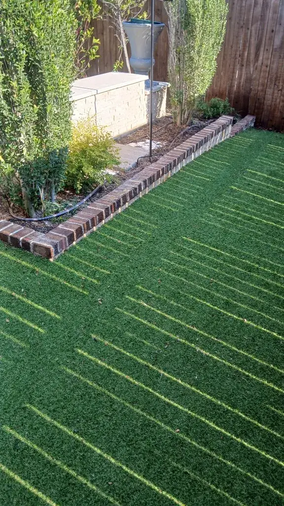 Finished even turf lawn with a dark brick garden border, mulched planting bed, and evergreen hedges