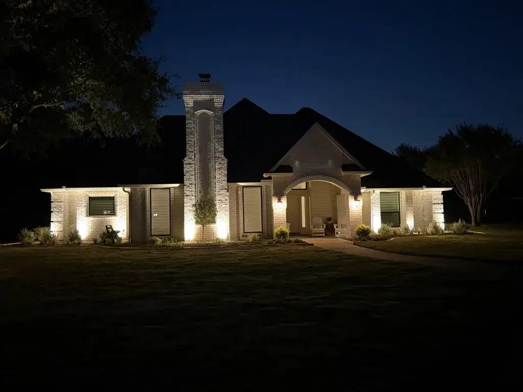 Southlake architectural lighting on a white brick home with chimney accents and a lit arched entry