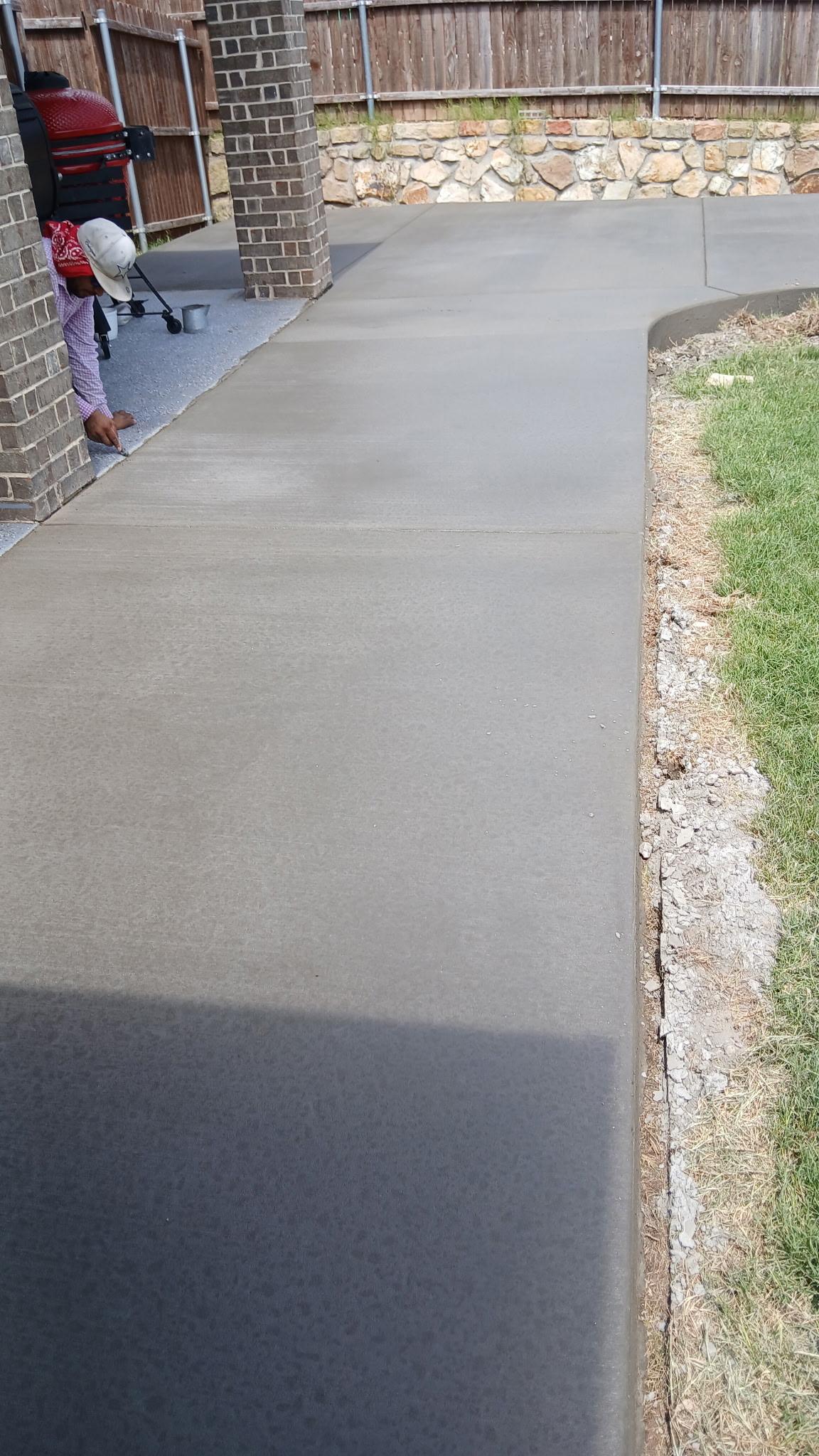 Freshly poured concrete walkway alongside a brick home
