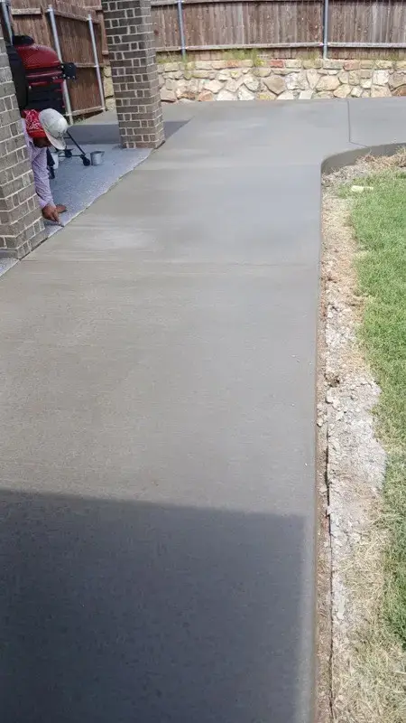 Freshly poured concrete walkway alongside a brick home