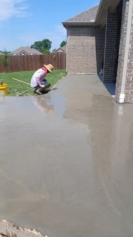 Crew hand-finishing a wet concrete slab next to a home